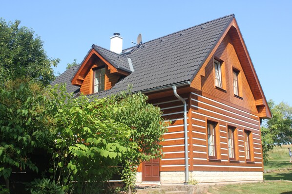 A log cabin with a steeply pitched roof, a chimney, and a large window.