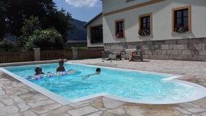 A swimming pool with stone tiles, a lounge area with chairs, and a mountain view.
