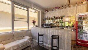 Zona de bar con sofá, dos taburetes, barra con botellas y refrigerador de Coca-Cola.
