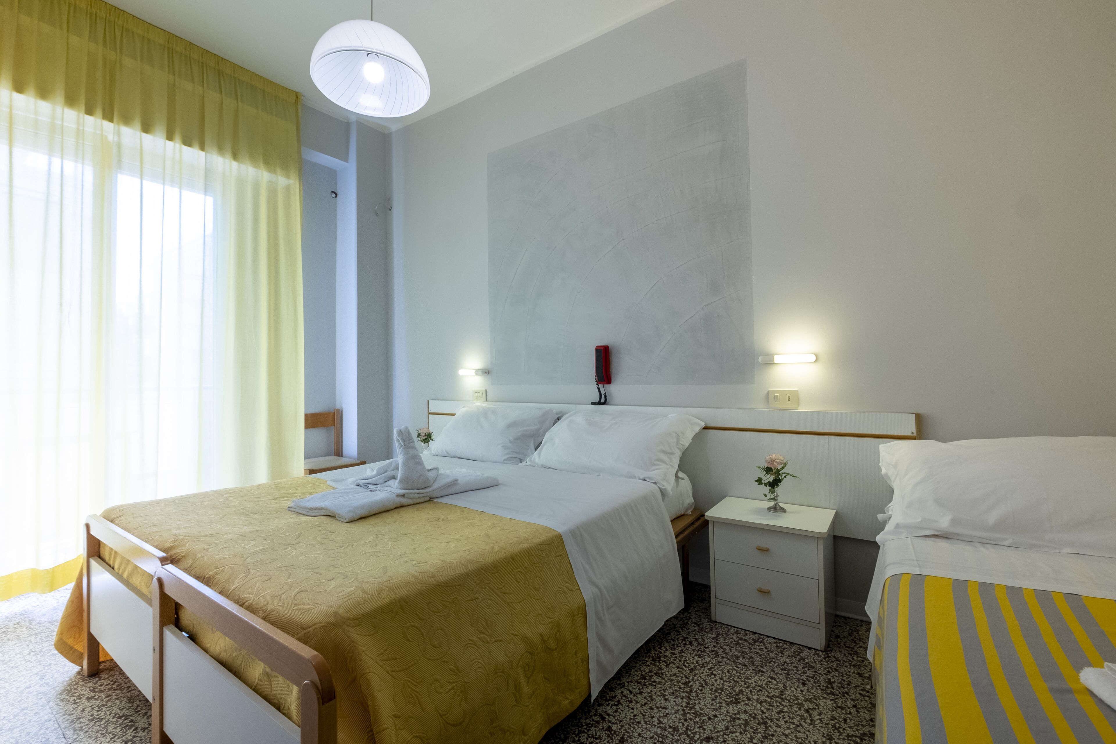 Una habitación de hotel con cama, mesita de noche, lámpara y ventana con cortinas.