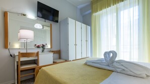 Una habitación de hotel con cama, escritorio, armario, espejo y televisor.