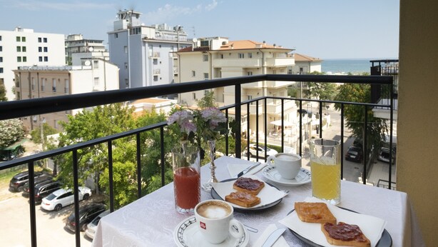 Un balcón con una mesa dispuesta para el desayuno, incluyendo tostadas, una bebida y una taza de café.