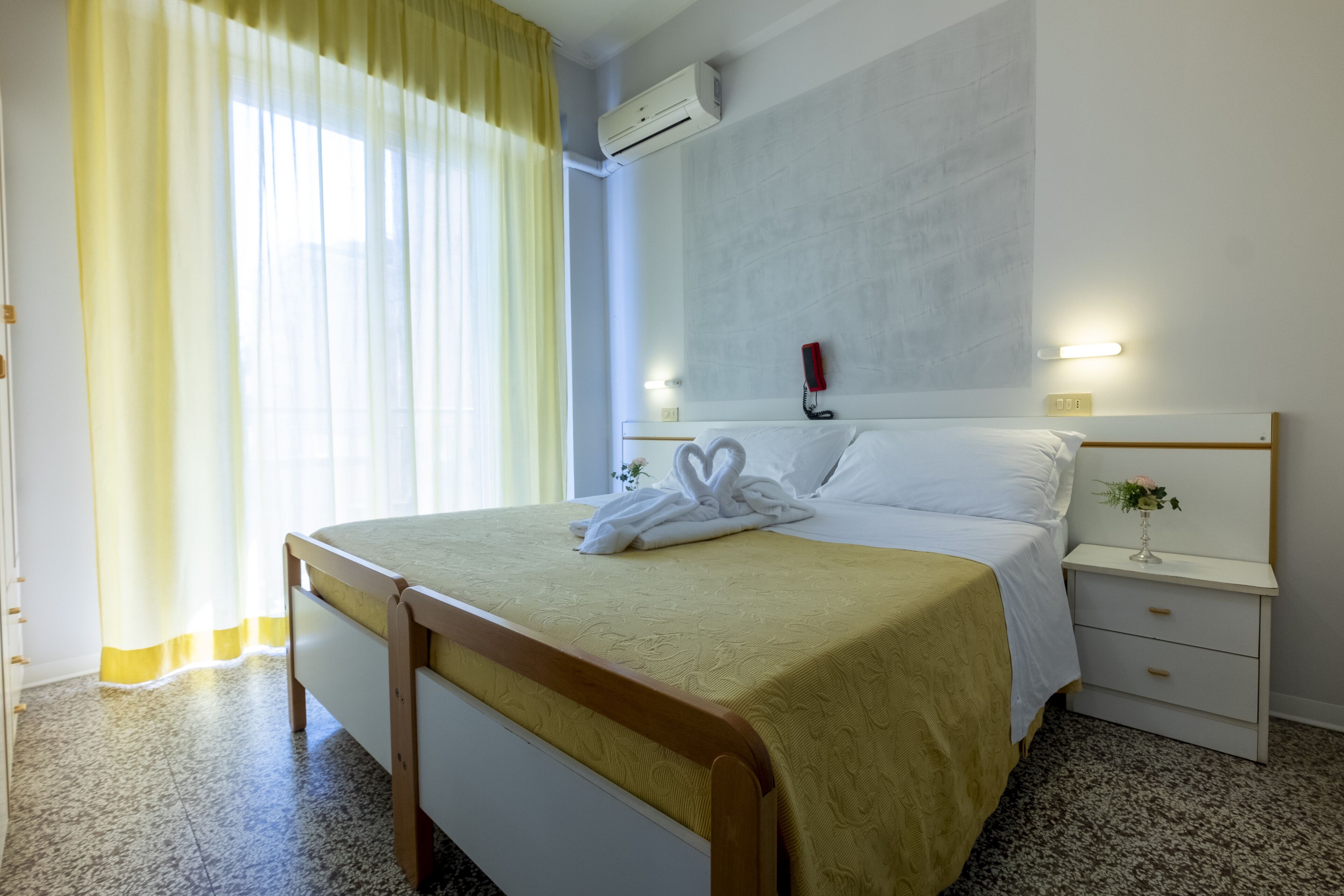 A hotel room with a bed, bedside table, and a wall-mounted phone.
