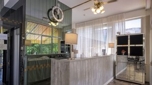 Un moderno vestíbulo de hotel con un mostrador de recepción de mármol, ventanas grandes con cortinas, un muro de vidrio y un ventilador de techo.