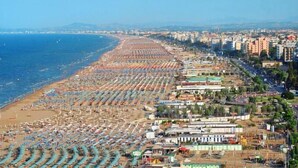 Un paisaje urbano costero con una playa extensa bordeada por hileras de sombrillas y tumbonas.