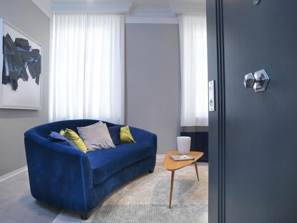 Una sala de estar moderna con un sofá azul, una mesita de madera y un florero blanco.