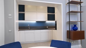 Una cocina moderna con armarios blancos, encimera negra y un florero azul sobre un estante de madera.