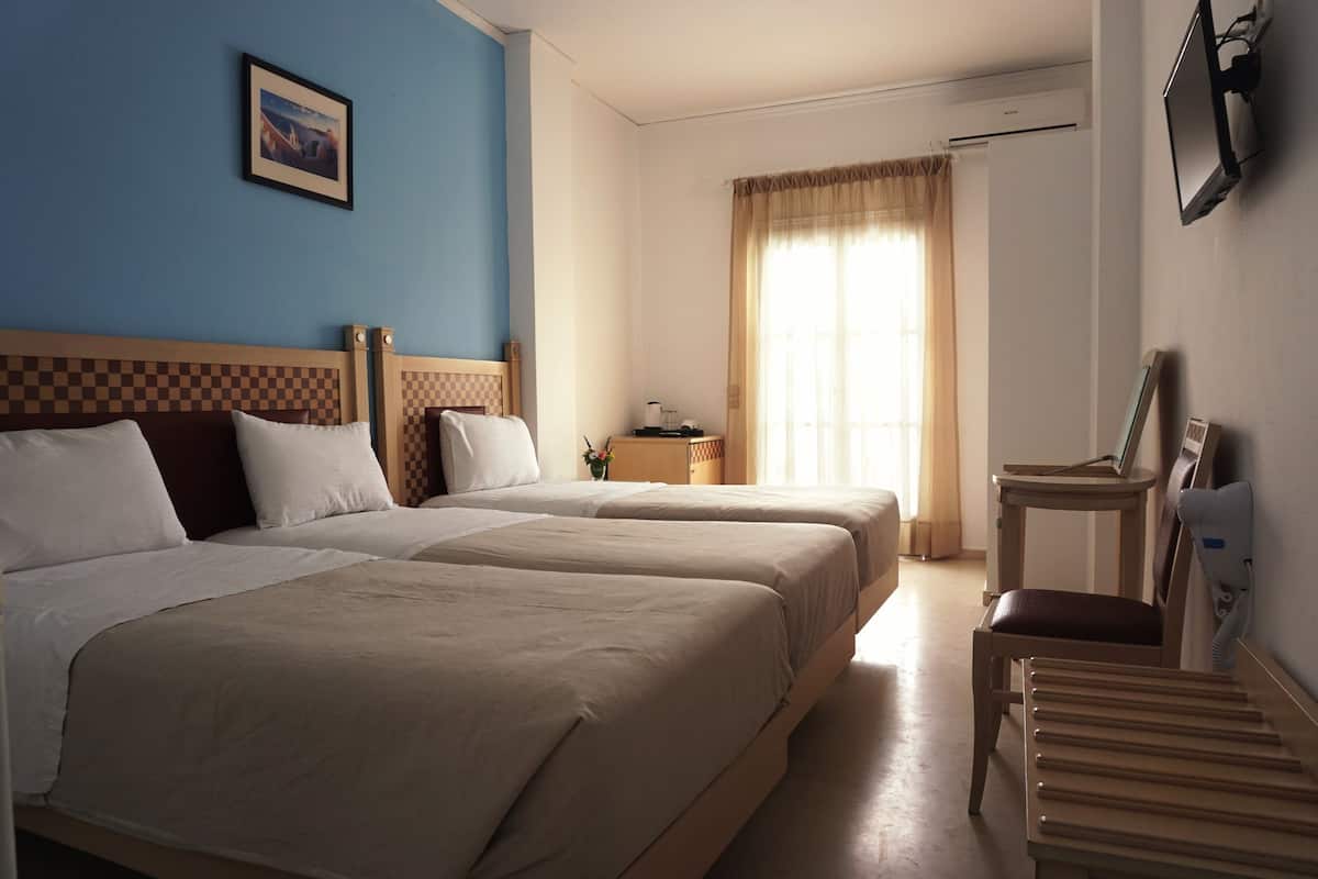 Quarto de hotel com duas camas, uma mesa pequena, uma cadeira, uma televisão e um quadro na parede.