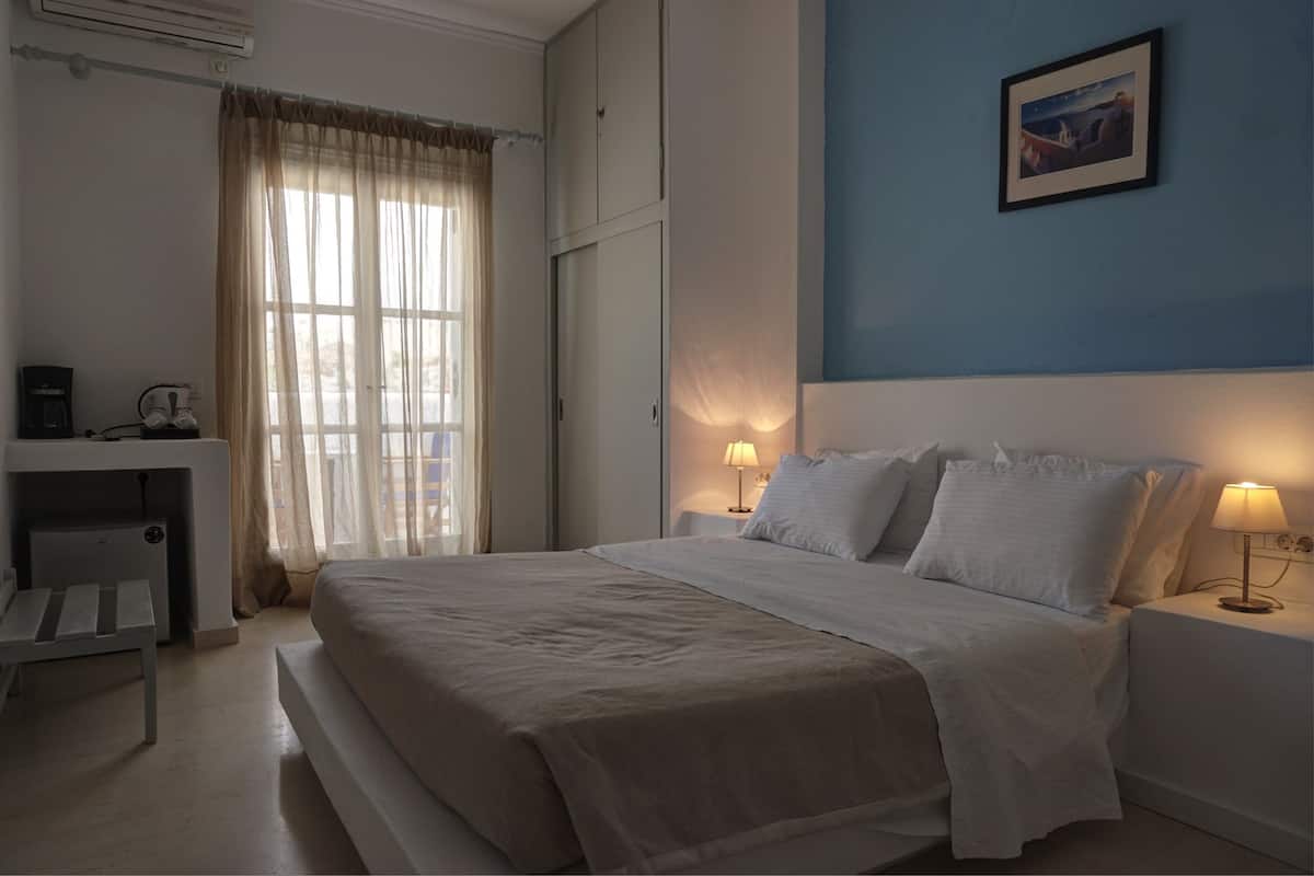 Quarto de hotel com cama, abajures, escrivaninha e cadeira, e janela com cortinas.
