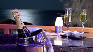 Una botella de Moët champagne, dos copas y una vela encendida sobre una mesa al aire libre con vistas al océano y la luna en el cielo.