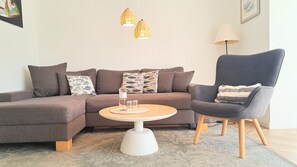 A modern living room with a sectional sofa, a round coffee table, a grey armchair, and two pendant lights.