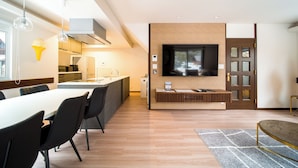 A modern kitchen with a dining area, a TV mounted on a brick wall, and a wooden door. - Yama House Hakuba (Hakuba)