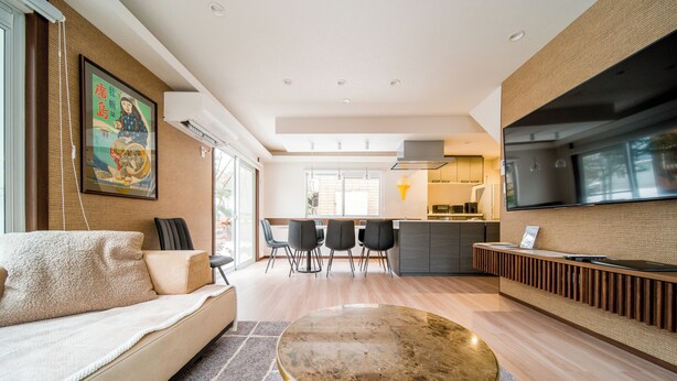 A modern living room with a sofa, a round coffee table, and a TV mounted on the wall. - Yama House Hakuba (Hakuba)