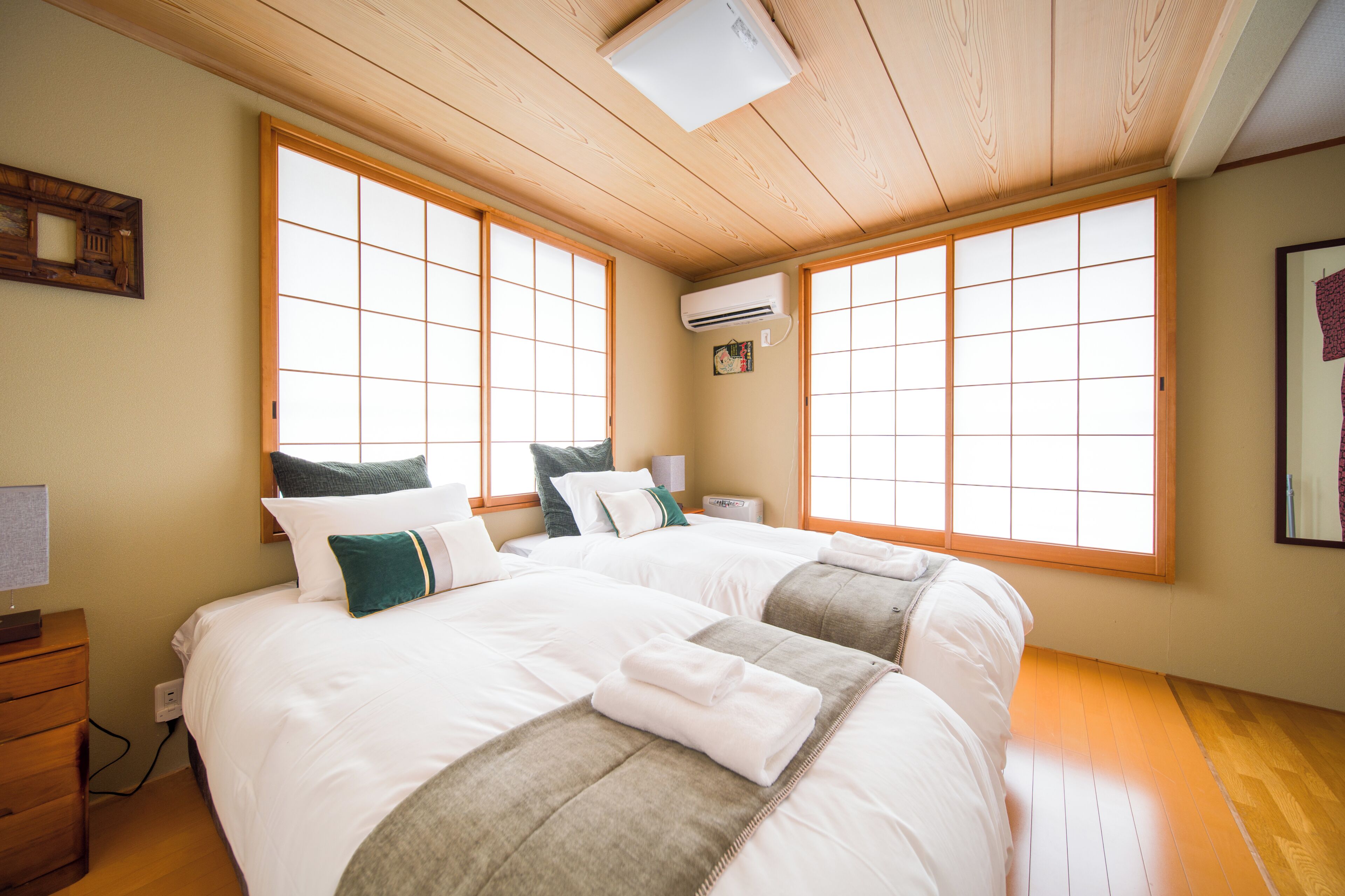 A hotel room with two beds, a wooden floor, and large windows.
