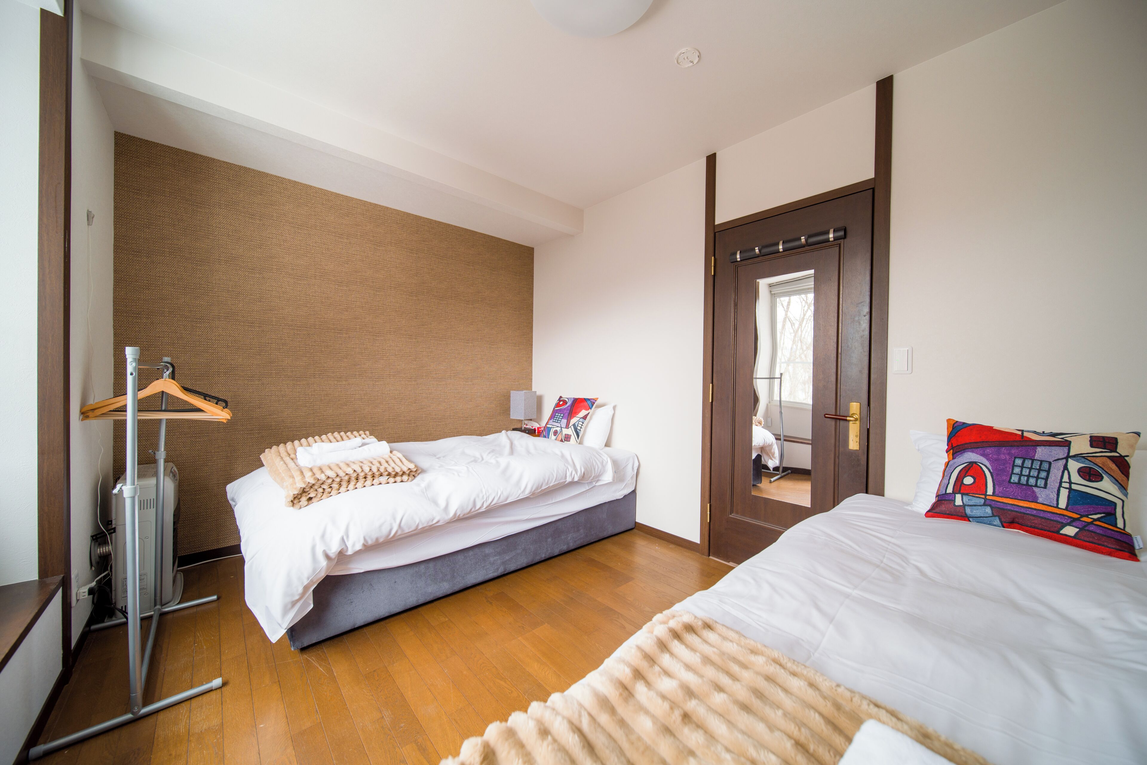 Quarto de hotel com cama, mesa de cabeceira, cabideiro e porta para outro espaço.