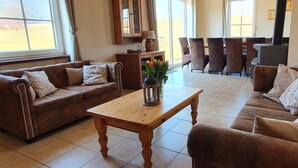 A living room with a brown leather sofa, a wooden coffee table, and a dining area with chairs and a table.