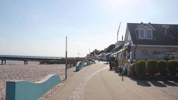 A coastal walkway with a beach, a pier, and a row of buildings including a restaurant. - Ostwind im Kirschgarten in Kellenhusen - Exclusive vacation apartment with sauna. (Kellenhusen)