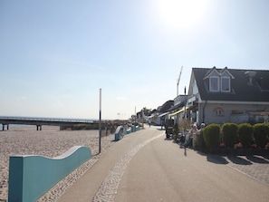 Une promenade en bord de mer avec une plage, une jetée et des bâtiments abritant des boutiques.