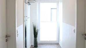 A hallway with a wooden floor, white walls, and a door at the end leading outside. - Ostwind im Kirschgarten in Kellenhusen - Exclusive vacation apartment with sauna. (Kellenhusen)