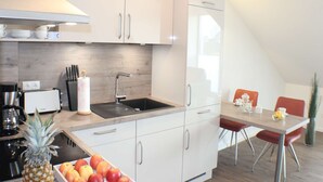 A modern kitchen with white cabinets, a black sink, and a dining area with a table and chairs. - Ostwind im Kirschgarten in Kellenhusen - Exclusive vacation apartment with sauna. (Kellenhusen)