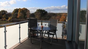 A balcony with a table and chairs, a bottle of wine, and a glass. - Ostwind im Kirschgarten in Kellenhusen - Exclusive vacation apartment with sauna. (Kellenhusen)