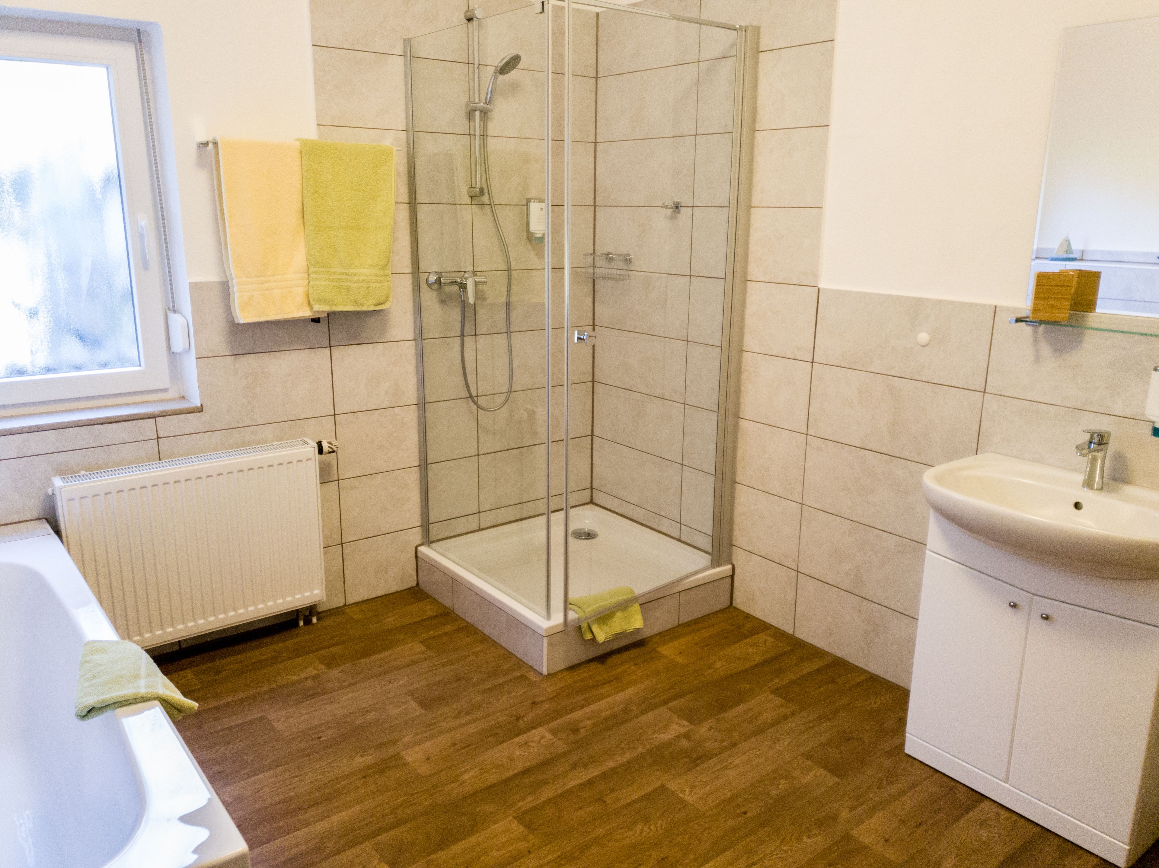 Une salle de bain avec une douche à parois de verre, un lavabo blanc et un plancher en bois.