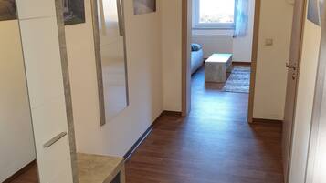 A hallway with wooden flooring, a bed, a window with curtains, and a door.
