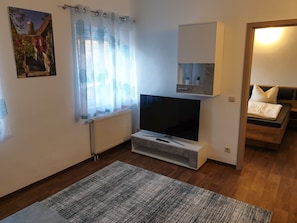 Una sala de estar moderna con un televisor de pantalla plana, un radiador, una alfombra estampada y una cama con cabecera.