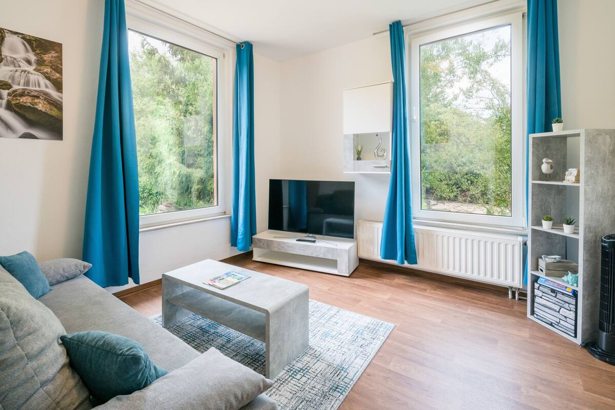 A modern living room with a grey sofa, a coffee table, a flat-screen TV, and a bookshelf.