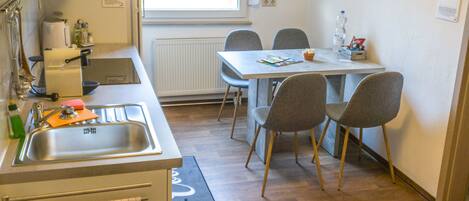 A compact kitchen with a sink, a window, and a dining area with chairs.