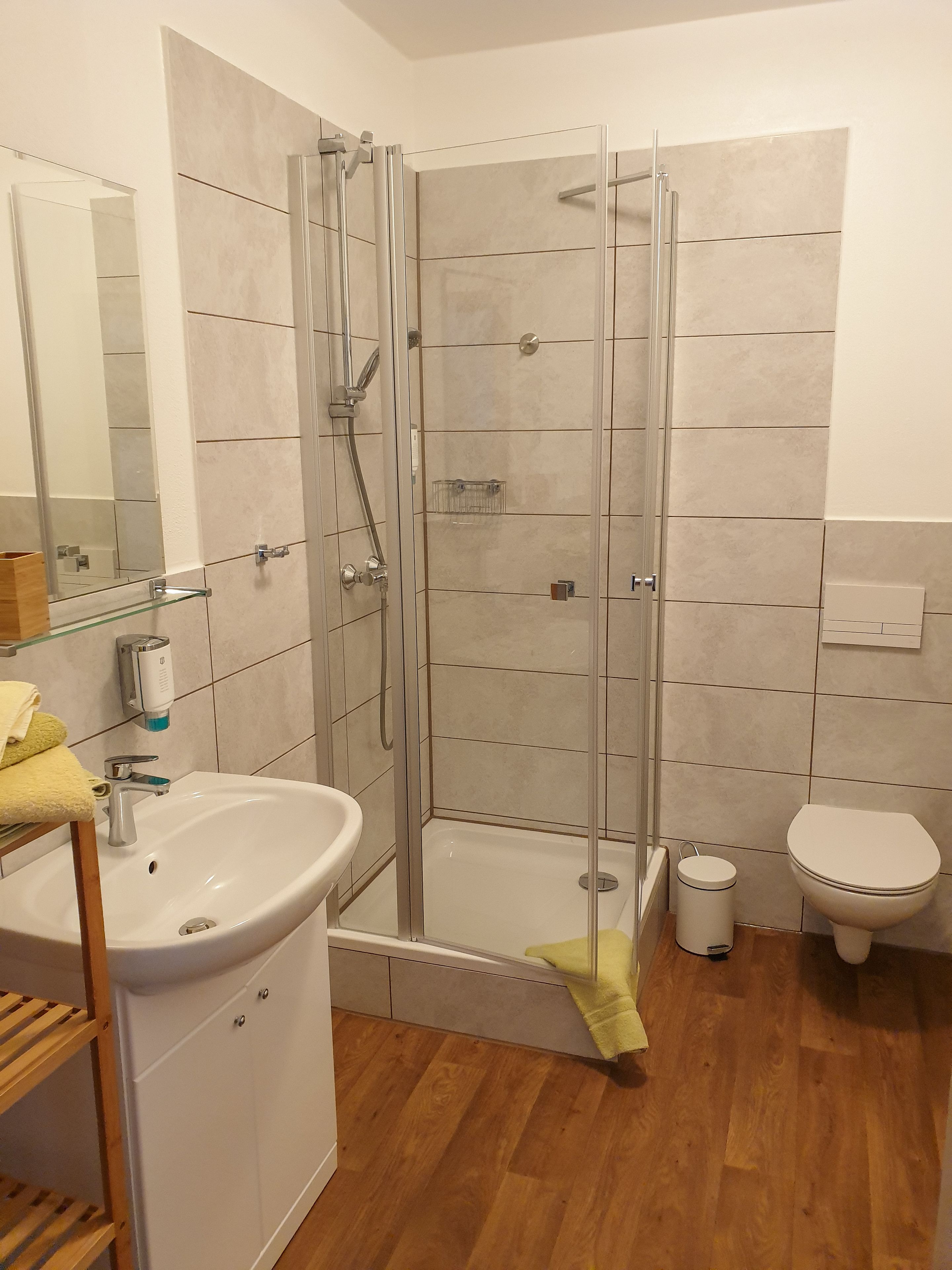 Un baño moderno con ducha de vidrio, lavamanos con espejo e inodoro.