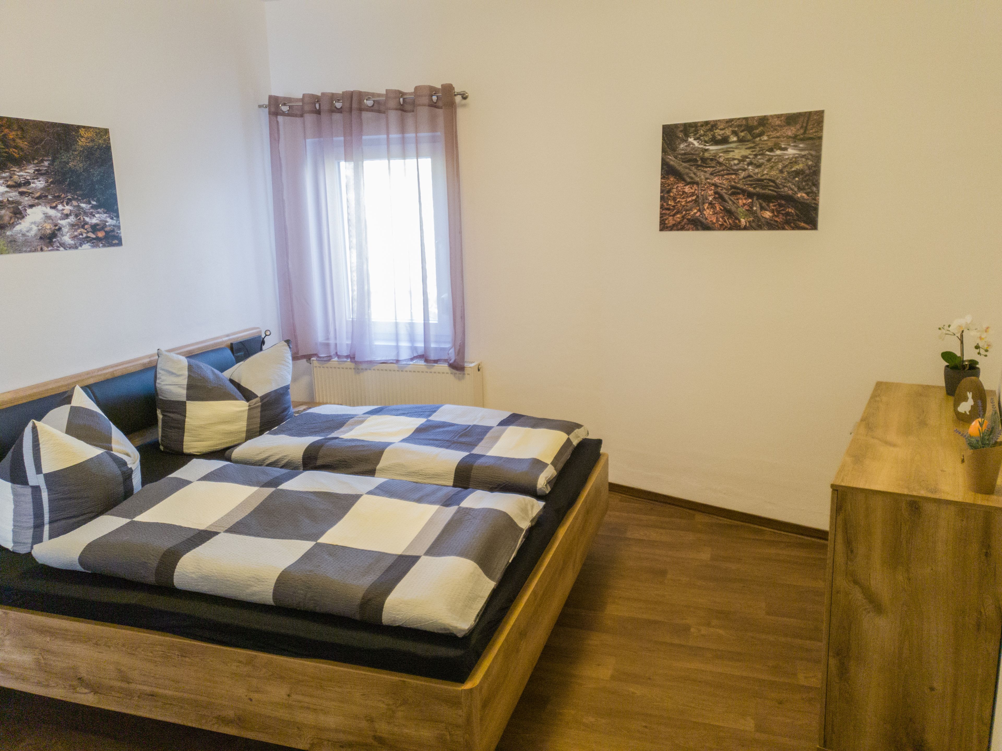 A bedroom with a bed, a wooden bedside table, and two framed pictures on the wall.