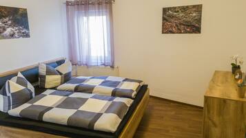 A bedroom with a bed, a wooden bedside table, and two framed pictures on the wall.