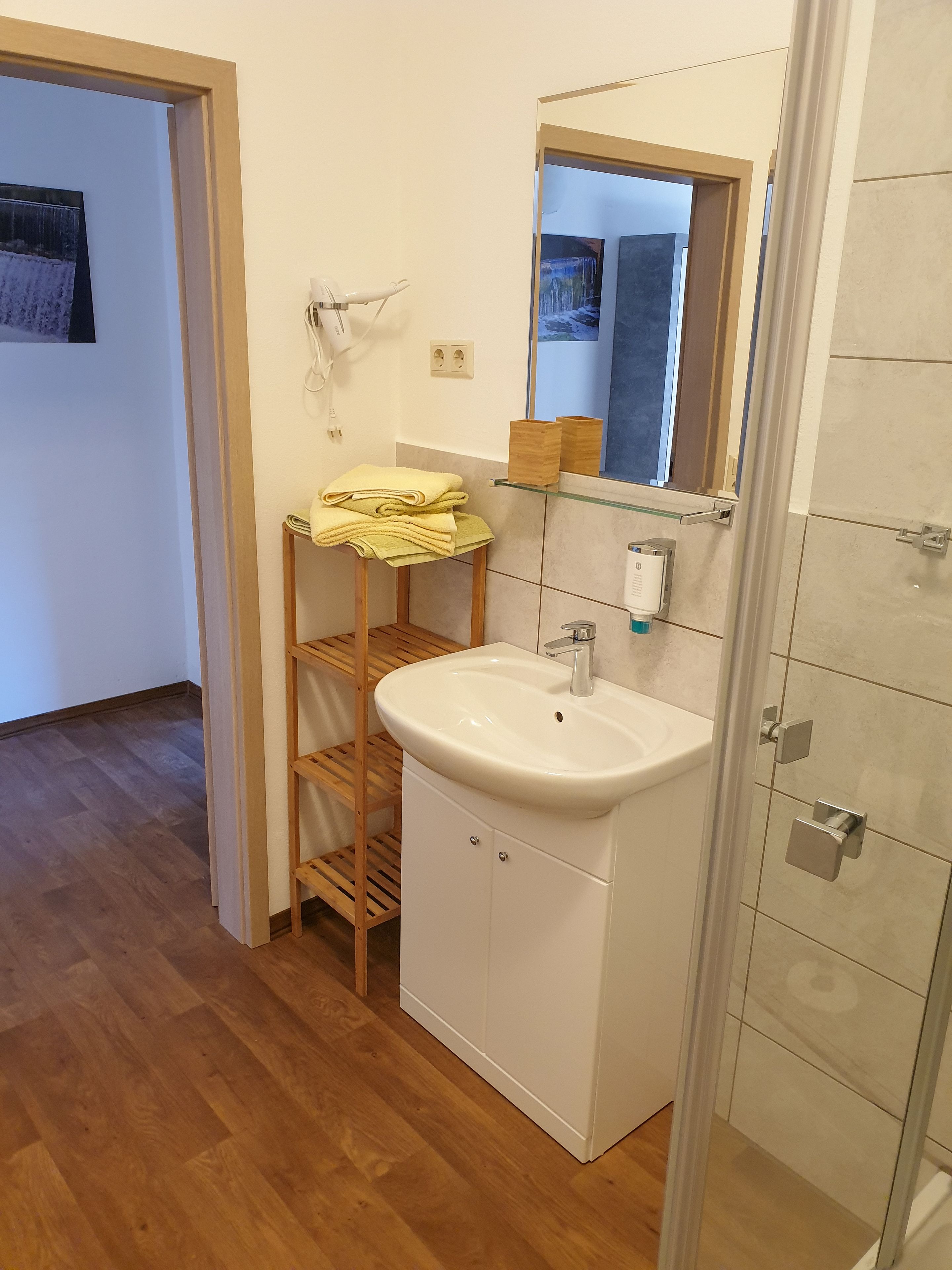 A bathroom with a white sink, wooden shelves, a mirror, and a shower area.