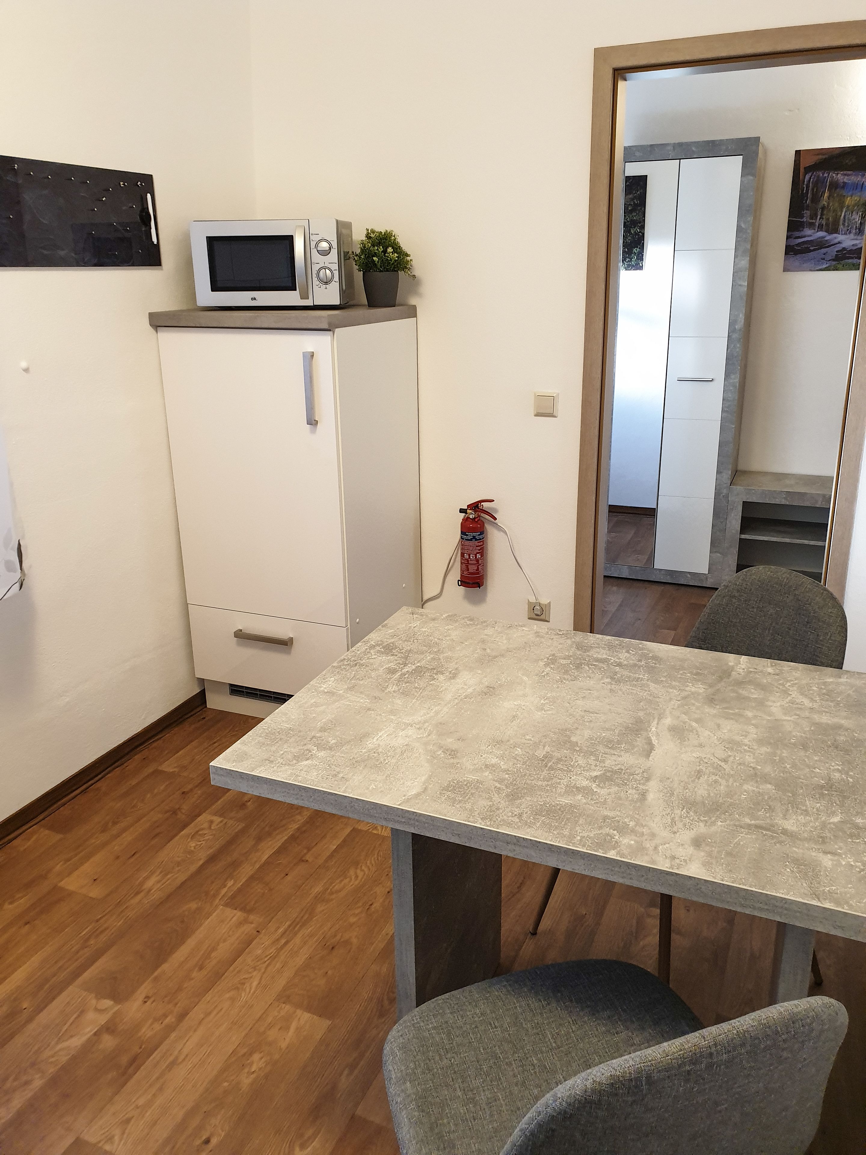 A compact kitchen with a microwave, a small refrigerator, and a fire extinguisher on the wall.