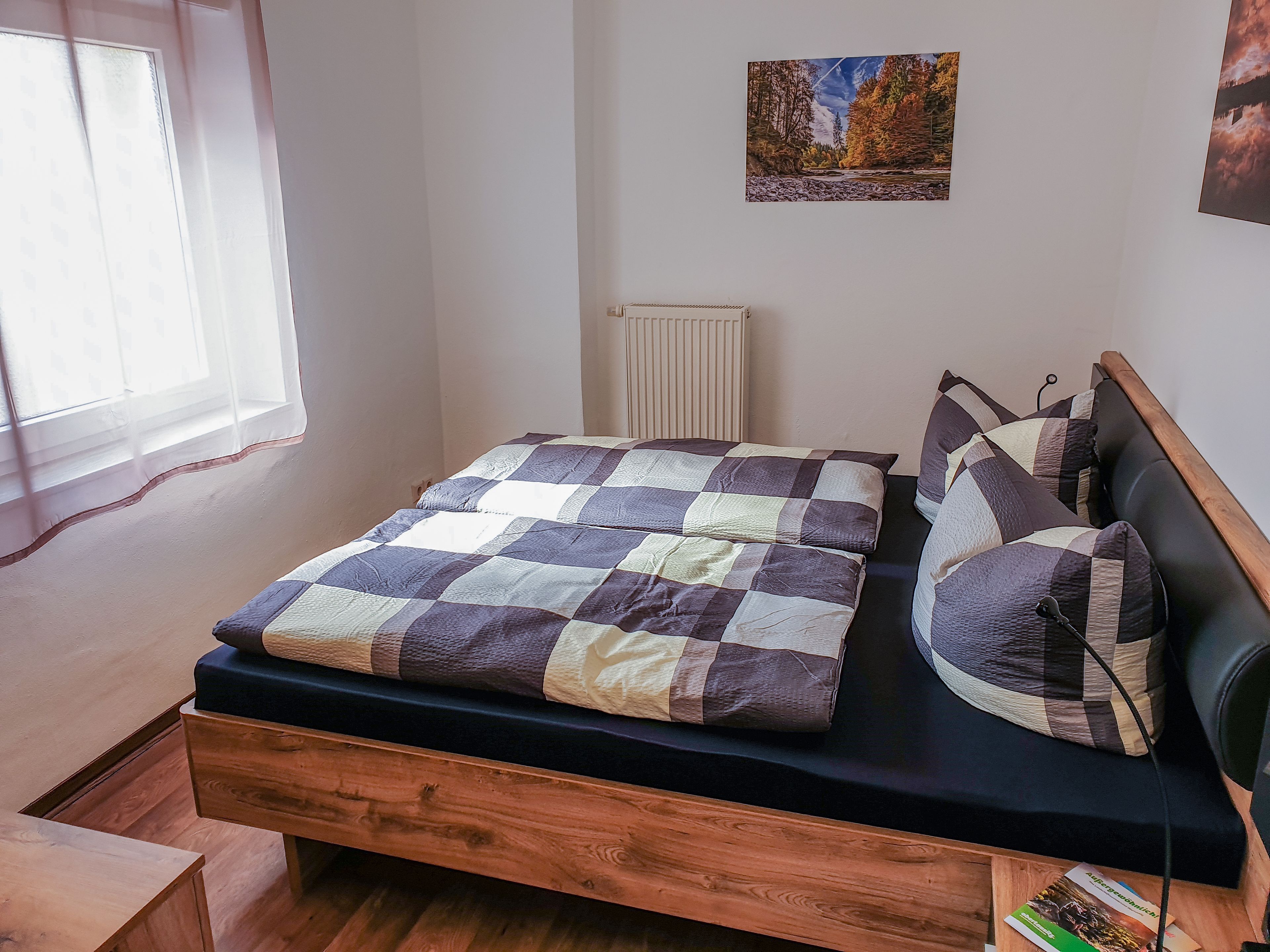 Une chambre à coucher avec un lit, une table de chevet en bois, un radiateur et une fenêtre avec des stores.