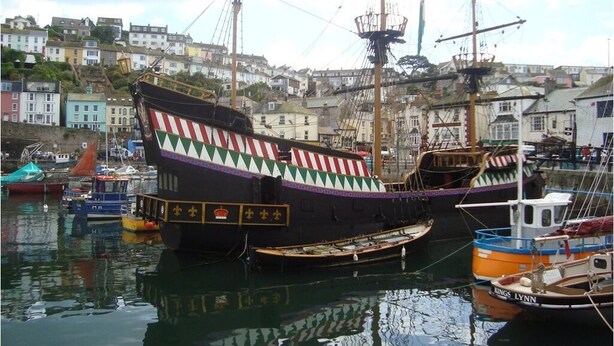 Un barco histórico amarrado en un puerto con edificios coloridos al fondo.