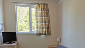 Un dormitorio con cama, escritorio con computadora, ventana con cortinas y lámpara.