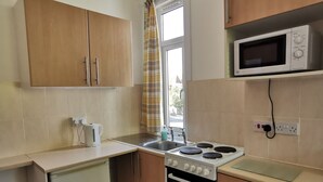Una cocina compacta con armarios de madera, un microondas, una estufa y un refrigerador pequeño.