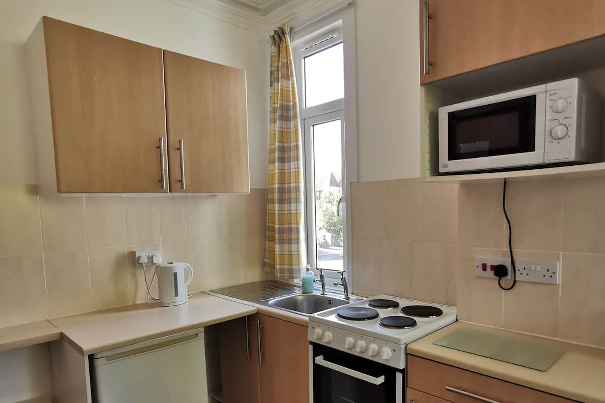 A compact kitchen with wooden cabinets, a microwave, a stove, and a small refrigerator.