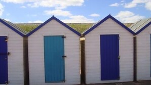 Una hilera de cabañas de playa con paredes blancas y puertas azules, dispuestas en línea recta.
