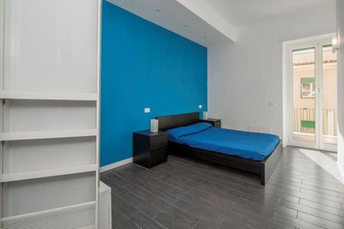 A bedroom with a bed, nightstands, a blue wall, and a balcony door.