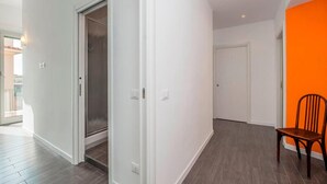 Un pasillo con una puerta corrediza de vidrio que da a un balcón, una puerta blanca y una silla frente a una pared naranja.