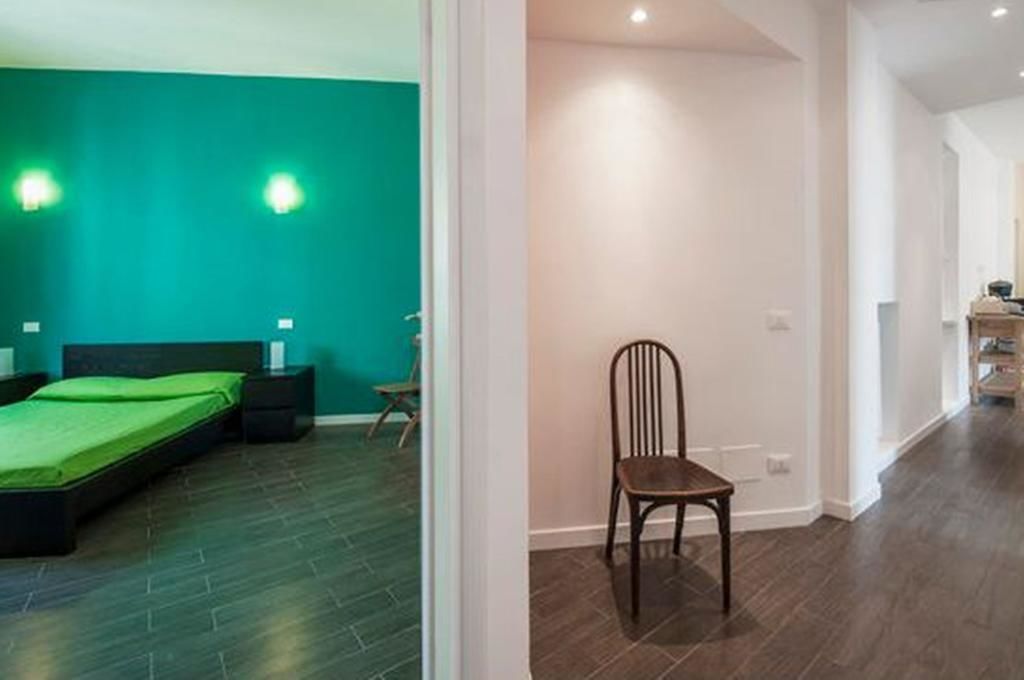 A modern bedroom with a green wall, a bed, a nightstand, and a chair.