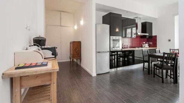 Una cocina moderna con armarios oscuros, un comedor con mesa y sillas de madera, y un pequeño escritorio de madera con una silla.