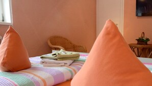 A bed with a striped blanket and two orange pillows, a wicker chair, and a small table with a plant. - Gaststätte & Pension  Zur Krone (Schimberg)