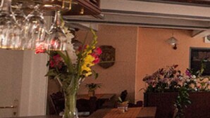 A dining area with a wooden table, chairs, and a vase with flowers. - Gaststätte & Pension  Zur Krone (Schimberg)
