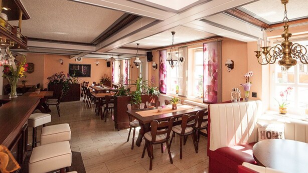 A spacious dining area with multiple tables and chairs, a bar area with stools, and a large window with curtains. - Gaststätte & Pension  Zur Krone (Schimberg)