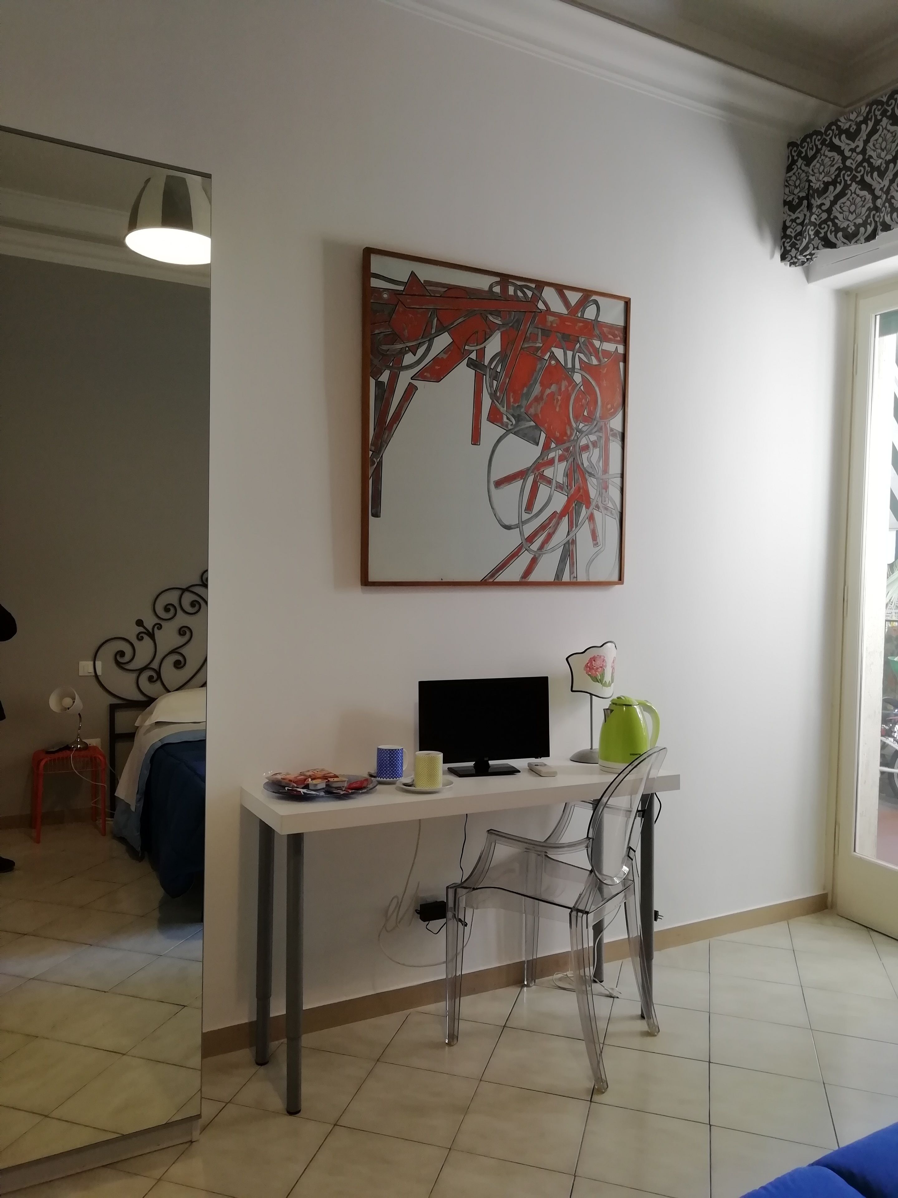 Una habitación con cama, escritorio con computadora, silla, lámpara y ventana con vistas.
