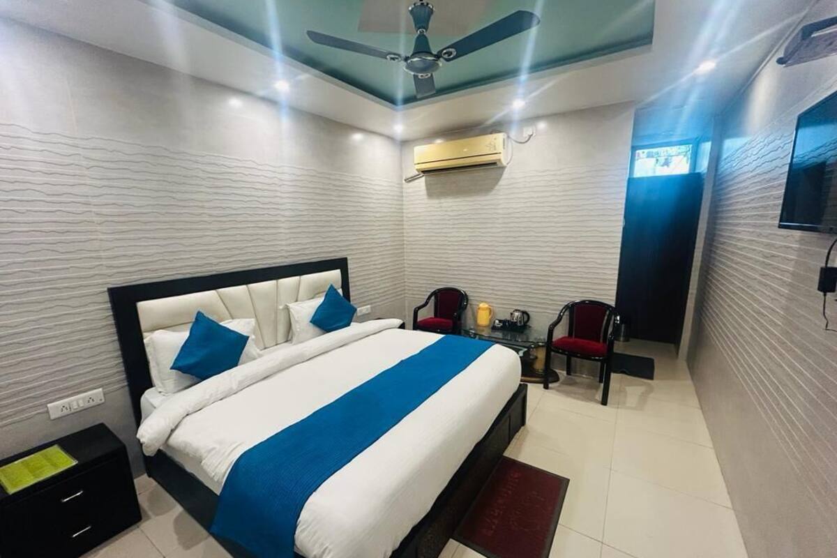 A modern hotel room with a large bed, a ceiling fan, an air conditioning unit, a TV, and a small seating area with chairs.